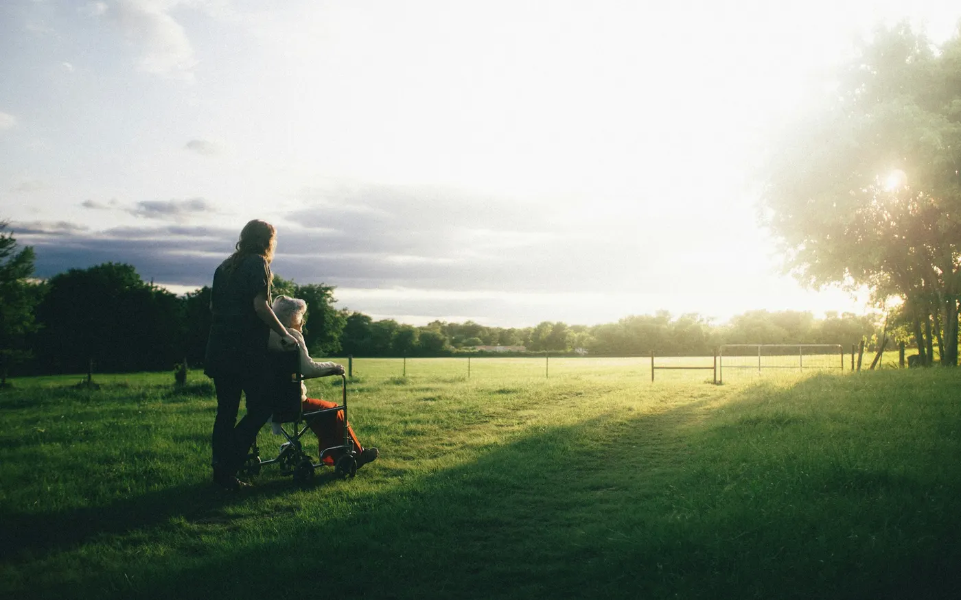 Personne en fauteuil roulant et son accompagnante dans un parc au coucher du soleil